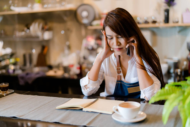 An Asian barista woman is stressed because of economic conditions and COVID-19 or Coronavirus has caused her sales in the coffee shop to drop dramatically, the impact of a small self-employed business - Фото, зображення