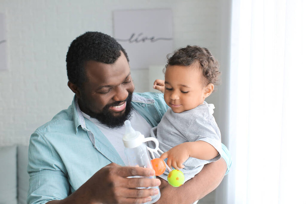 Hombre afroamericano dando agua a su lindo bebé en casa
 - Foto, imagen