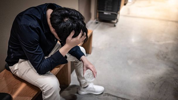 Asiatische Geschäftsleute fühlen sich gestresst und deprimiert, während sie auf der Bank sitzen. Männliche Büroangestellte mit Migräne-Kopfschmerzen durch Kündigung und Wirtschaftskrise. Depression aus unternehmerischem Problemkonzept - Foto, Bild