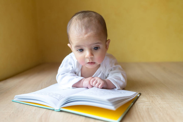 Novorozené dítě s knihou. Malý chlapec v bílém obleku. Krásný portrét batolete. Dítě s velkýma očima. Vzdálené vzdělání. Vzdálenost učení - Fotografie, Obrázek
