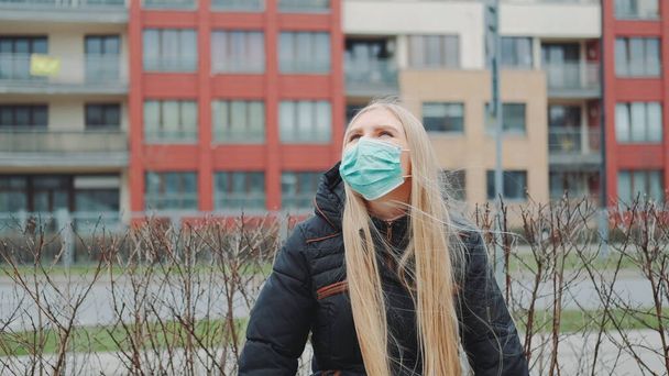 Menina loira em uma máscara médica sentada no banco
. - Foto, Imagem