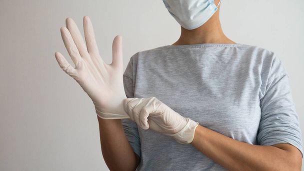 Kobieta w masce zakładająca białe jałowe rękawice chirurgiczne.. - Zdjęcie, obraz