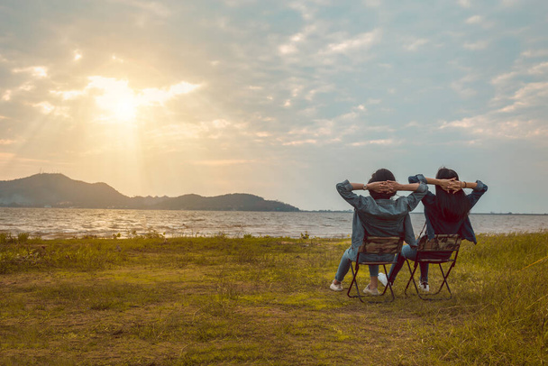 Vrienden vrouwen zitten rust in de buurt van de berg na wandelen of kamperen samen bij zonsondergang. - Foto, afbeelding
