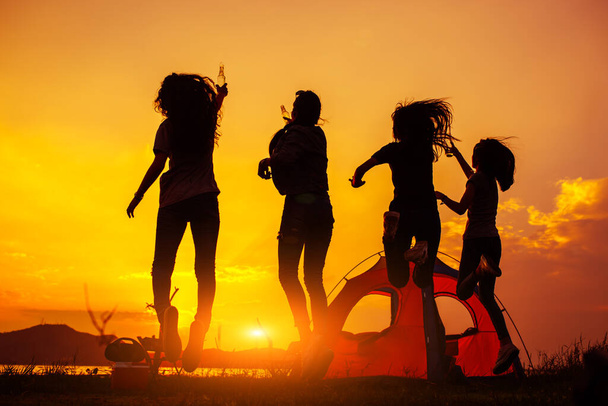 Siluetti Ryhmä naisia puolue juomapulloja ja hyppäämällä nauttia matkustaa retkeily, vaellus lomalla aikaa auringonlaskun
. - Valokuva, kuva