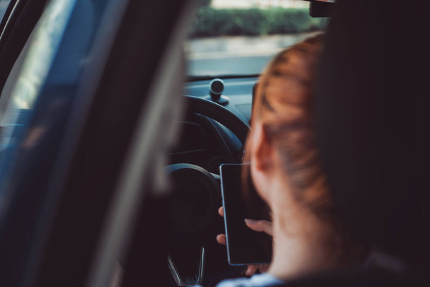 Vrouw met mobiele smartphone tijdens het rijden gevaar en risico op ongevallen concept, kopieer ruimte de linker stuurwiel selectieve focus. - Foto, afbeelding