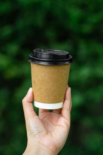 woman holding a paper coffee cup mockup on nature green blurred background.vertical image - Photo, Image