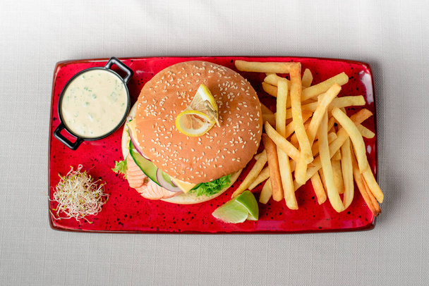 Hambúrguer com salmão e batatas fritas com molho
 - Foto, Imagem