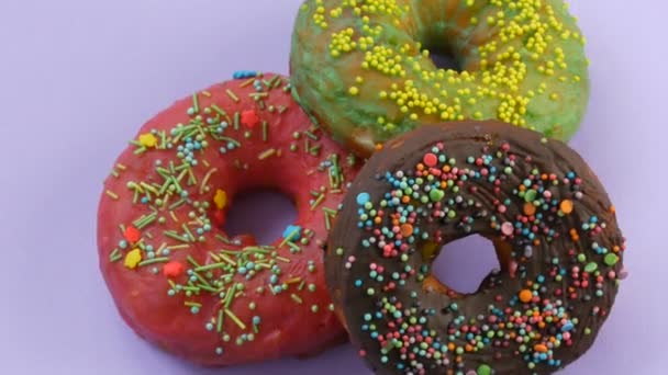 American donuts with colorful glaze and powder. Rotate on a violet background close up view - Footage, Video