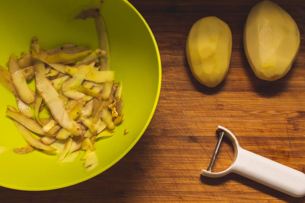 Cutting board with a potato and peeler and a bowl with potato skin - Photo, Image