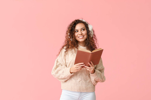 Young woman in warm sweater and with book on color background - Photo, image