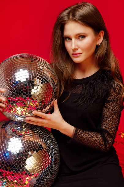 meisje met heldere make-up houdt een disco bal op een rode achtergrond close-up - Foto, afbeelding