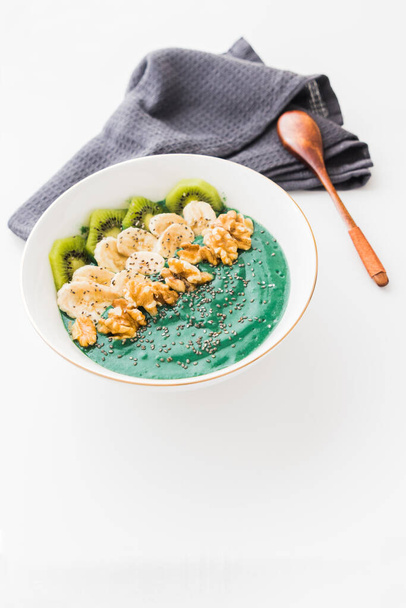 A spirulina smoothie bowl with banana, walnuts, kiwi and chia seeds on white background - Foto, immagini