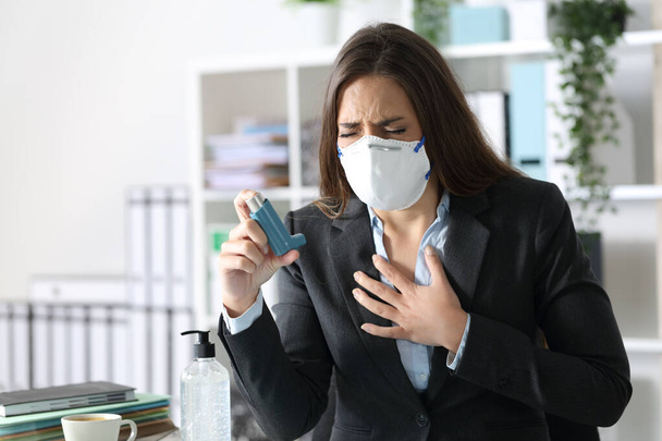 Executive woman wearing protective mask with asthma attack holding inhaler touching chest at the office - Foto, Bild