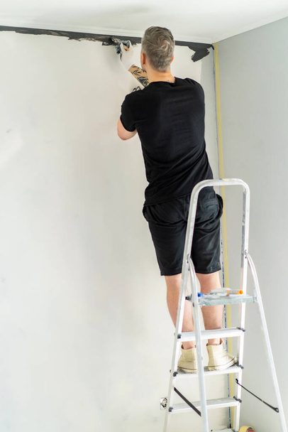 repairs. the man paints the walls with a roller, prepares for painting, repairs in the room. repaint the wall. - Fotó, kép