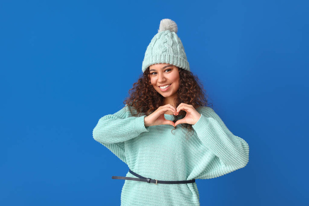 Young woman in warm sweater making heart shape with hands on color background - Foto, immagini