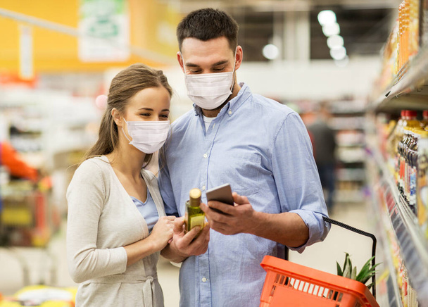 couple in masks with phone and olive oil at store - Photo, image