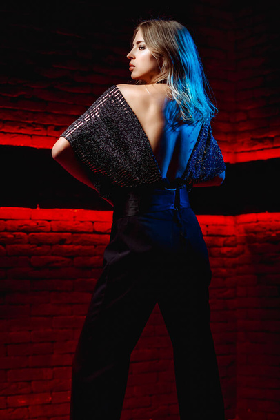 Schöne Mädchen Modell in Neonlicht. Junge Frau in einem Kleid mit offenem Rücken in Rot mit blauem Licht in einem Club - Foto, Bild