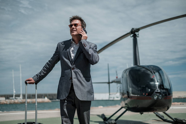 Liikemies puhuu puhelimessa lähellä yksityistä helikopteria
 - Valokuva, kuva