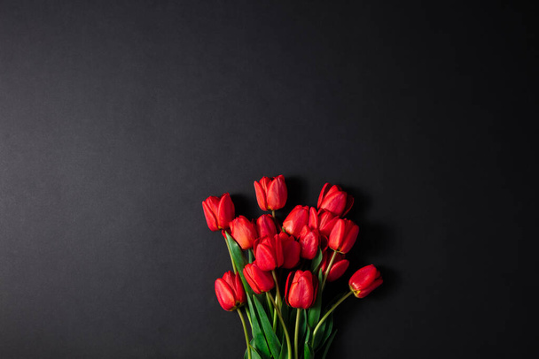Coloque el texto cerca del ramo de tulipanes rojos frescos sobre un fondo negro. Un gran ramo de flores frescas de primavera sobre una mesa oscura
. - Foto, imagen