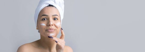 Ritratto di bellezza della donna in asciugamano bianco sulla testa applica crema al viso. Detergente per la pelle eco biologico cosmetico spa relax concept. - Foto, immagini