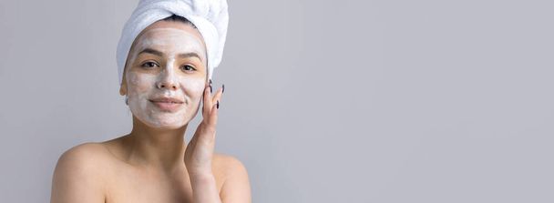 Piękny portret kobiety w białym ręczniku na głowie nakłada krem na twarz. pielęgnacja skóry oczyszczanie ekologiczne kosmetyki spa relaks koncepcja. - Zdjęcie, obraz