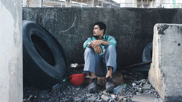 У стены сидит азиатский бездомный. Его лицо полно страданий, депрессии и отчаяния. Люди безработные из-за последствий вспышки коронного вируса
. - Фото, изображение