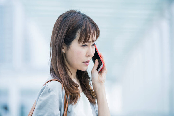 Asiatische Geschäftsfrau ruft mit beunruhigtem Gesichtsausdruck ein Smartphone an - Foto, Bild