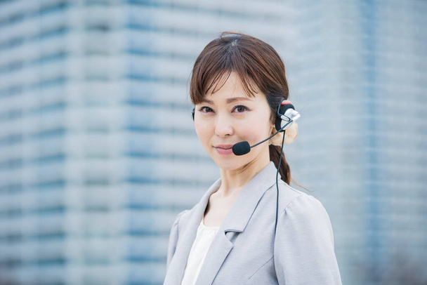 Azji (japoński) operator kobieta nosi słuchawki z mikrofonem w dzielnicy biznesowej - Zdjęcie, obraz