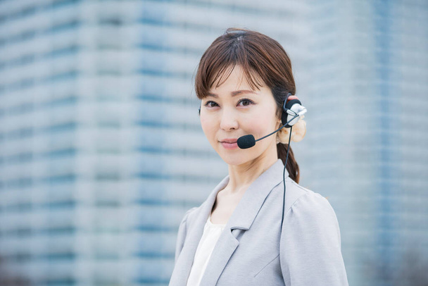 Ázsiai (japán) női operátor mikrofonnal felszerelt fejhallgatóval az üzleti negyedben - Fotó, kép