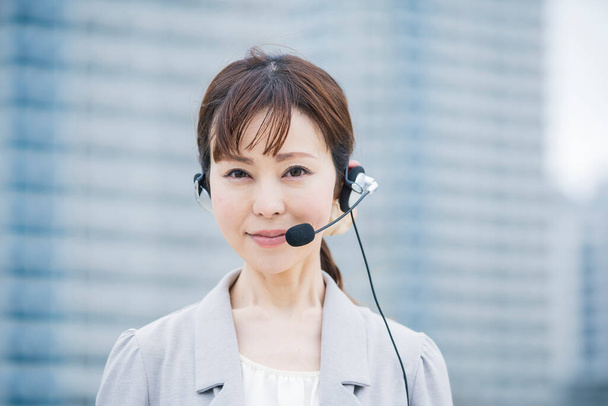 ビジネス街にマイク付きヘッドフォンを装着するアジア系女性事業者 - 写真・画像