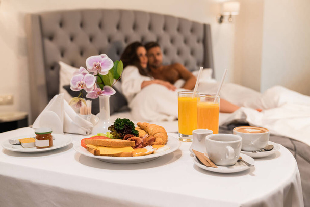 Podnos se snídaní, pokojová služba, mladé páry mají líbánky v hotelu - Fotografie, Obrázek