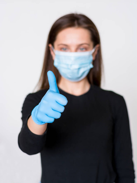 Junge Frau in medizinischer Maske und Handschuhen zeigt Daumen nach oben. Quarantäne - Foto, Bild