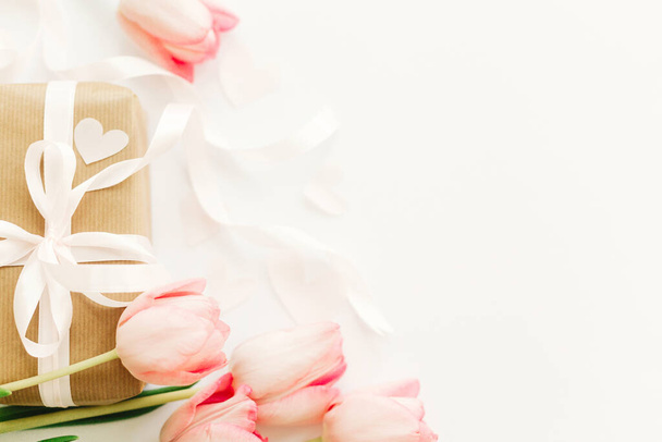 Tulipanes rosados con cinta y caja de regalo sobre fondo blanco, posición plana. Elegante imagen tierna. Tarjeta de felicitación con espacio para texto. Feliz día de San Valentín. Boda o maqueta de San Valentín. Feliz día de las mujeres
 - Foto, imagen