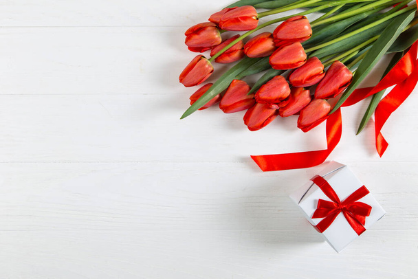 Red tulips and a gift on white table. Mother's Day copy space. - Foto, Imagen