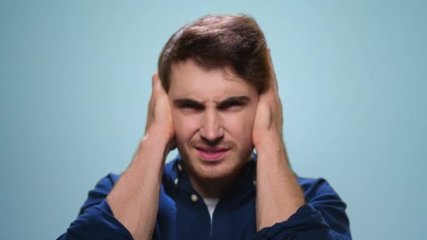 Mężczyzna trzymający się za głowę na niebieskim tle. Student mający stres w studio - Materiał filmowy, wideo
