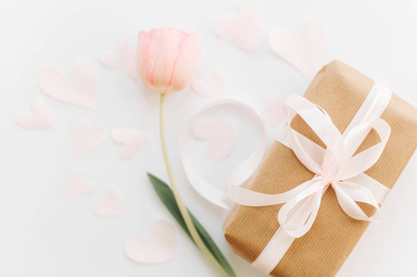 Caja de regalo con cinta y tulipán rosa plano sobre fondo blanco, espacio para el texto. Elegante imagen de primavera suave. Feliz día de las mujeres. Tarjeta de felicitación maqueta. Feliz Día de las Madres. Día de San Valentín romántico
 - Foto, Imagen