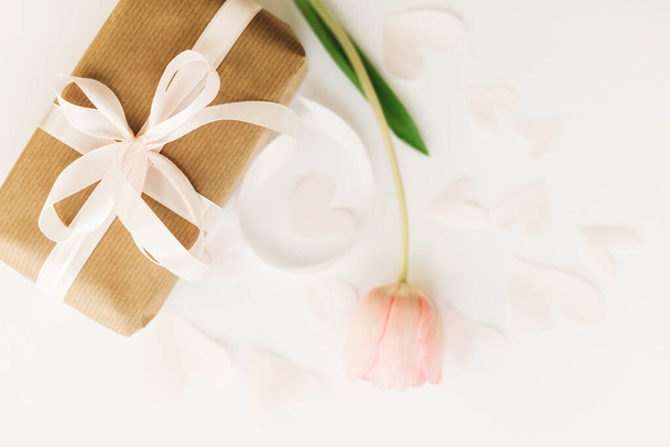 Boldog nőnapot! Ajándék doboz szalaggal és rózsaszín tulipán lapos feküdt fehér háttér, hely a szöveg. Stílusos lágy tavaszi kép. Üdvözlőlap mockup. Boldog Anyák Napját. Romantikus Valentin nap - Fotó, kép