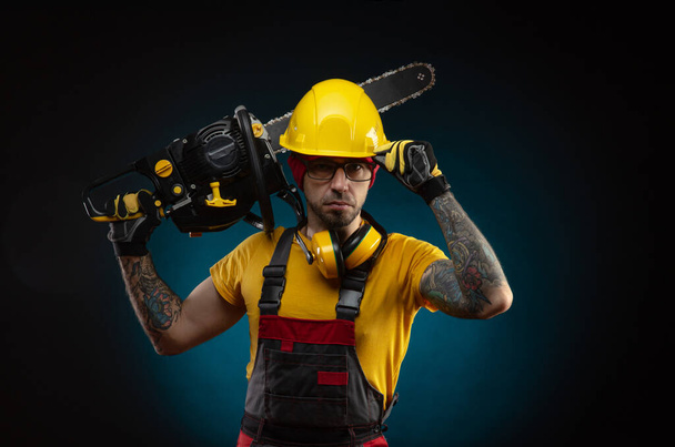 a guy in protective overalls with a chainsaw on a dark background - Foto, imagen