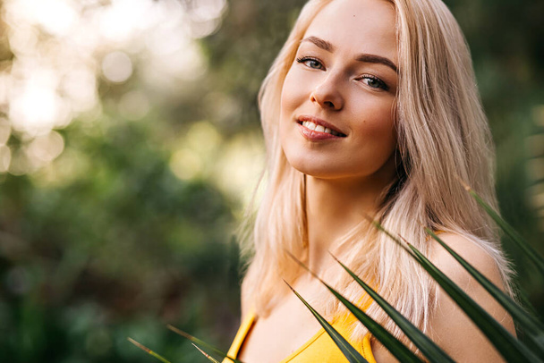 Closeup vertical portrait of happy beautiful luxurious blonde with cute smile standing near palm tree on the beach, wearing bright swimsuit, relaxing on tropical island. Vacation, travel, summer. - Φωτογραφία, εικόνα