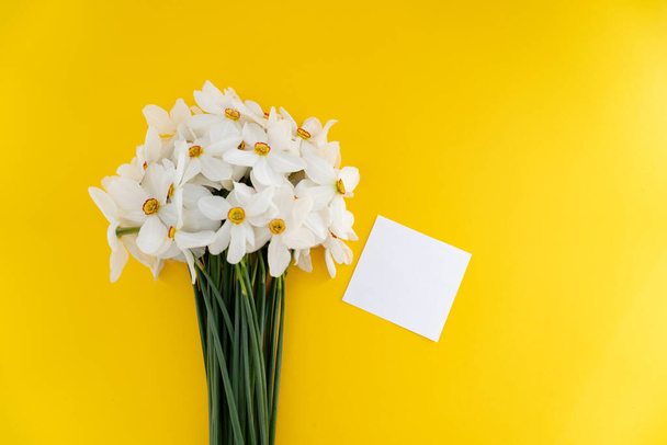 Closeup of fresh white daffodils bouquet with white paper blank note - Фото, изображение