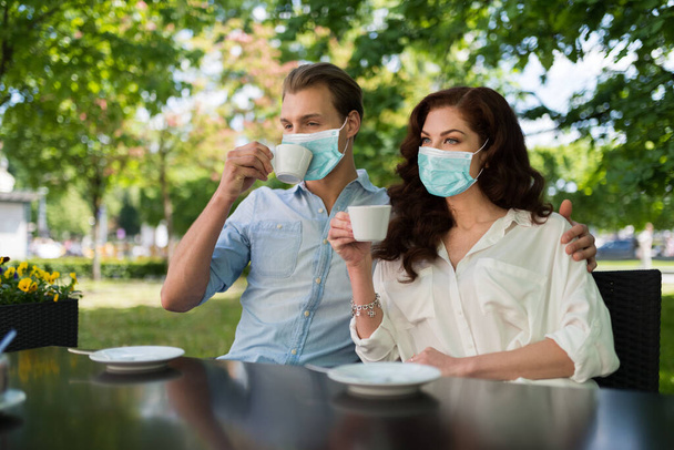 Young couple drinking a tea together outdoor while wearing a mask, funny coronavirus pandemic concept - Photo, image