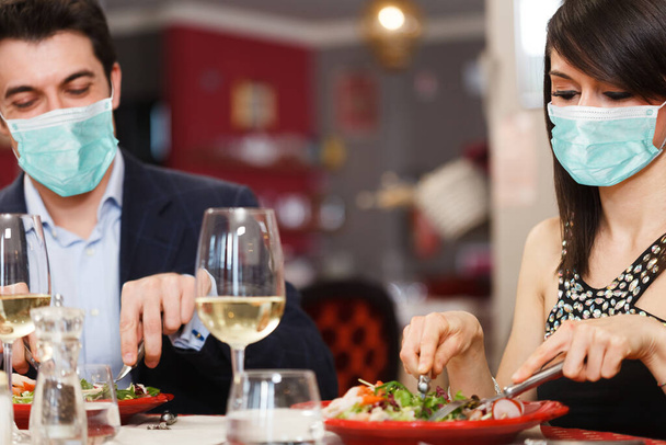 Masked couple having dinner in a restaurant, funny coronavirus concept - Zdjęcie, obraz