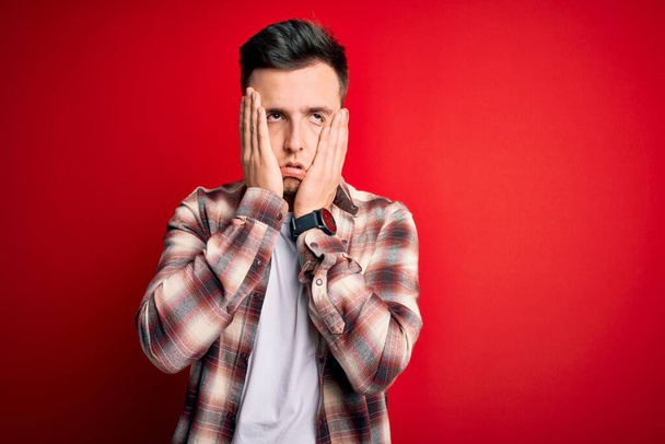 Young handsome caucasian man wearing casual modern shirt over red isolated background Tired hands covering face, depression and sadness, upset and irritated for problem - Фото, зображення