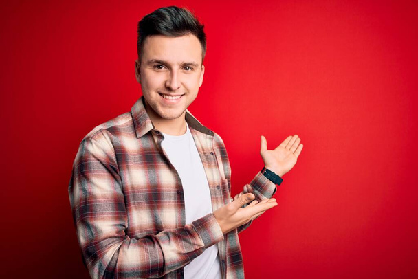 Young handsome caucasian man wearing casual modern shirt over red isolated background Inviting to enter smiling natural with open hand - Фото, зображення