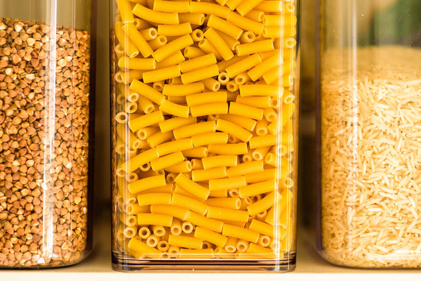 сира макаронна паста, гречка та басматі рис всередині прозорого контейнера для зберігання на кухонній полиці
 - Фото, зображення