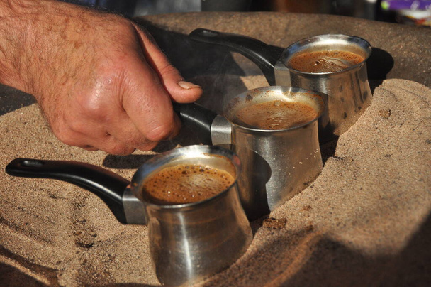 Arab kávé főtt réz fém tégelyben forró homokban az egyik utcai standon Aqaba, Jordan. Kávé íze kardamommal és cukorral 1 jordániai dinár számára. - Fotó, kép