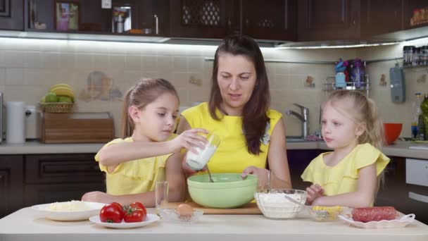 Máma a její dvě dcery se baví v kuchyni. Máma učí děti, jak dělat pizzu. Šťastná matka a šťastné děti vaří večeři společně v kuchyni. - Záběry, video