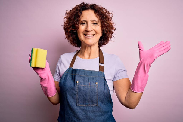 家事をしている中年の巻き毛の女性は、エプロンと手袋を使用して家事を掃除します非常に幸せと興奮,大きな笑顔で叫んで勝利を祝う勝者の式と上げ手 - 写真・画像