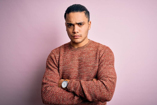 Jonge Braziliaanse man met casual trui over geïsoleerde roze achtergrond sceptisch en nerveus, afkeurende uitdrukking op gezicht met gekruiste armen. Negatief persoon. - Foto, afbeelding