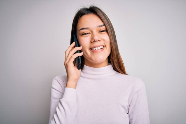 mooi brunette meisje hebben gesprek praten op de smartphone over witte achtergrond met een gelukkig gezicht staan en glimlachen met een zelfverzekerde glimlach tonen tanden - Foto, afbeelding